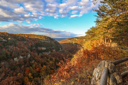 A scenic view of a valley surrounded by autumn foliage under a partly cloudy sky.
