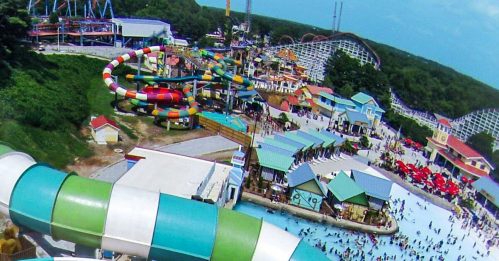 Aerial view of colorful water slides at a water park, with a large pool and many visitors enjoying the attractions below.