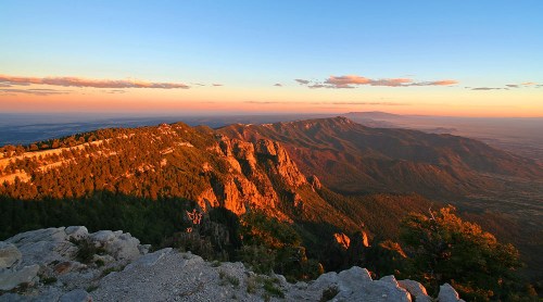 A scenic view of mountains at sunset, with warm light illuminating the rocky terrain and distant peaks.