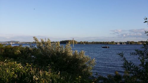 A serene river scene with lush greenery, a boat on the water, and a clear blue sky in the background.