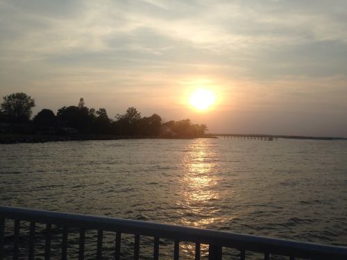 A serene sunset over a calm body of water, with silhouettes of trees and a distant pier.