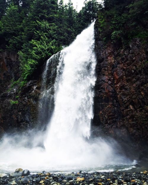 A powerful waterfall cascading down a rocky cliff, surrounded by lush green trees and mist rising from the base.