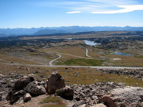 A panoramic view of rolling hills, winding roads, and distant mountains under a clear blue sky.