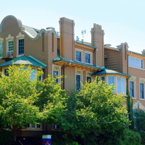 A large, historic building with a green roof, surrounded by lush trees and greenery on a sunny day.