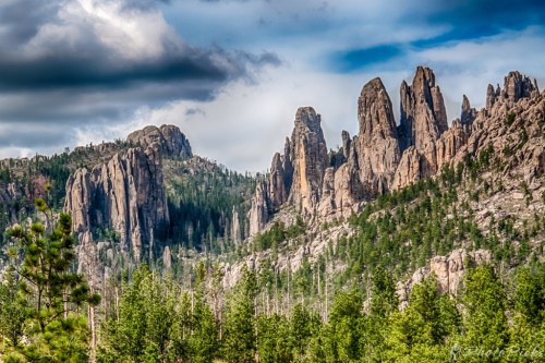 A rugged mountain landscape with towering rock formations and lush green trees under a cloudy sky.