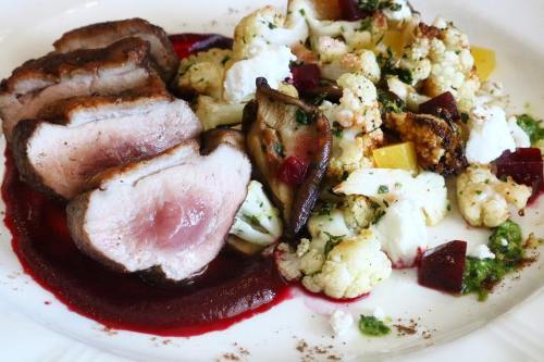 Sliced duck breast on a plate with roasted cauliflower, beets, and a berry sauce.