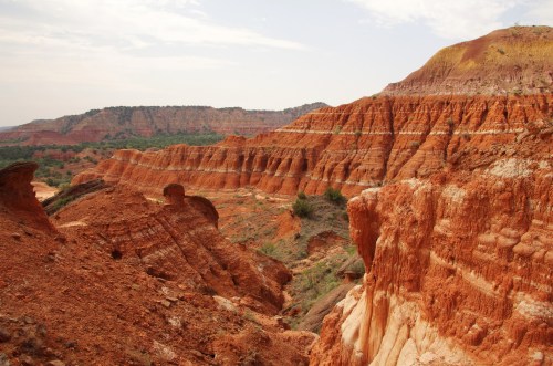 A scenic view of layered red rock formations and rugged terrain under a cloudy sky.