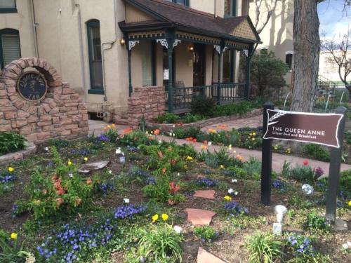 A charming bed and breakfast with a landscaped garden featuring colorful flowers and a sign for "The Queen Anne."