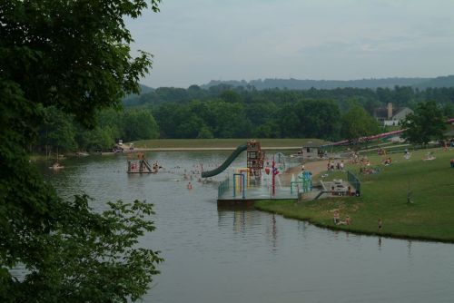 A scenic view of a lake with people swimming, a water slide, and grassy areas for relaxation.