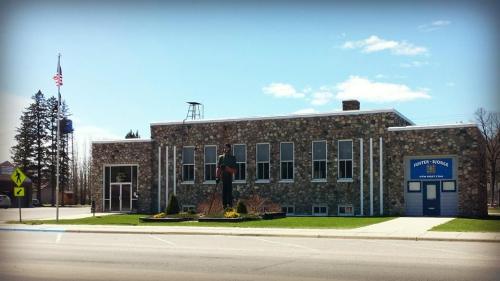 A stone building with large windows, a statue in front, and an American flag, set against a clear blue sky.