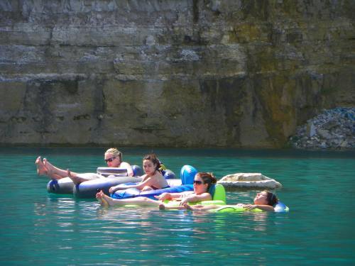 Four people relax on inflatable rafts in clear blue water, with a rocky cliff in the background.