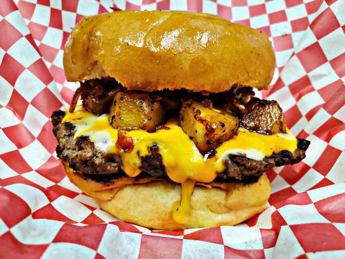 A juicy burger with melted cheese and grilled pineapple chunks, served in a toasted bun with a red and white checkered wrapper.