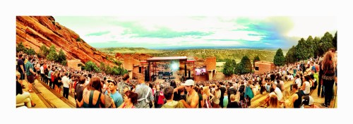 A panoramic view of a crowded outdoor concert at Red Rocks, surrounded by stunning rock formations and greenery.