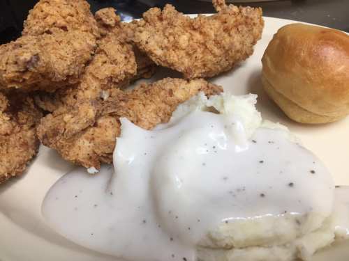 A plate of crispy fried chicken, creamy mashed potatoes with gravy, and a soft dinner roll.