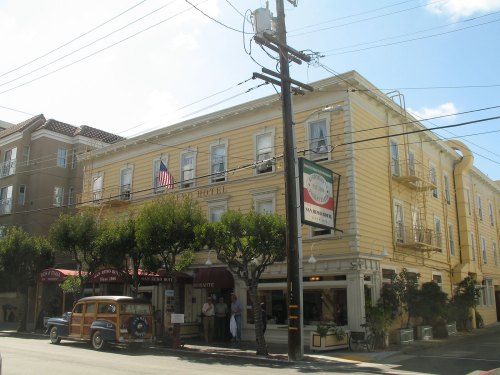 A yellow hotel building with an American flag, vintage car parked outside, and trees lining the street.