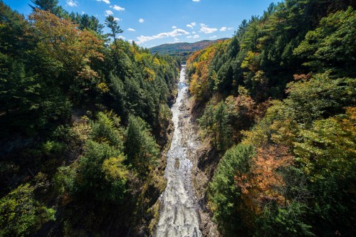 A scenic view of a river winding through a colorful forested canyon under a clear blue sky.