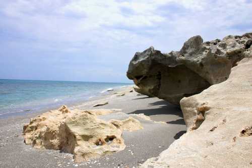 A rocky beach with large boulders and gentle waves under a cloudy sky.