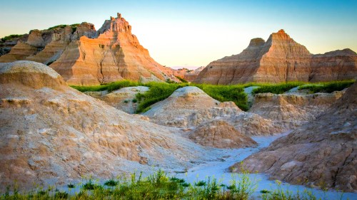 A scenic view of rugged, colorful rock formations and grassy areas under a clear sky at sunset.