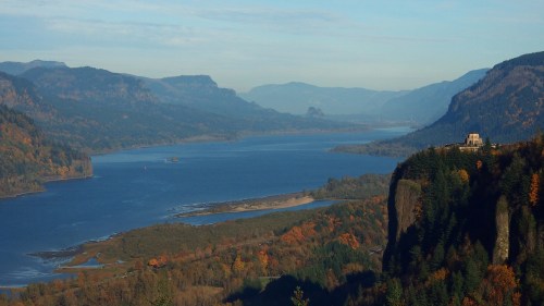 A scenic view of a river winding through mountains, with autumn foliage and a distant building on a cliff.