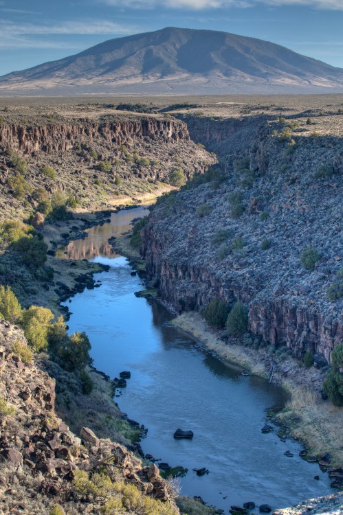 A serene river flows through a rocky canyon, with a distant mountain under a clear sky.