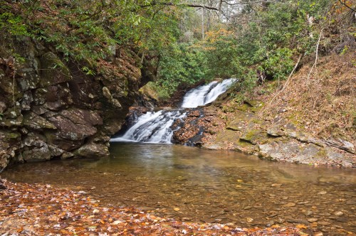 A serene waterfall cascades into a clear pool, surrounded by rocky terrain and autumn foliage.
