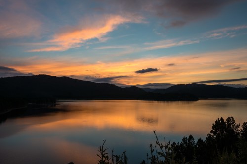 A serene lake at sunset, reflecting colorful clouds and mountains in the background.