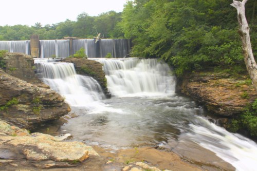 A serene waterfall cascading over rocky ledges, surrounded by lush green trees and a tranquil river.