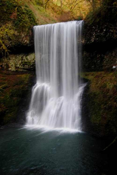 A serene waterfall cascading over rocks into a tranquil pool, surrounded by lush greenery.
