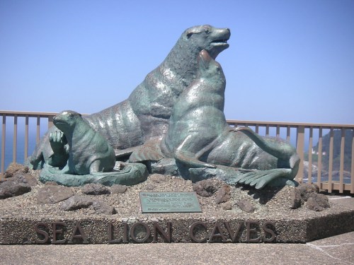 Bronze sculpture of sea lions resting on rocks, with a plaque labeled "Sea Lion Caves" in the foreground.