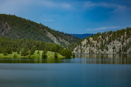 A serene lake surrounded by lush green hills and trees under a clear blue sky.