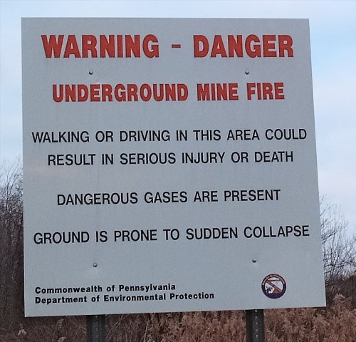 Sign warning of an underground mine fire, highlighting risks of injury, dangerous gases, and ground collapse.