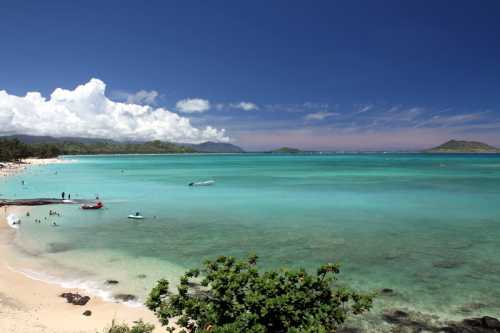 A scenic beach with turquoise waters, white sand, and people enjoying the sun under a blue sky with fluffy clouds.