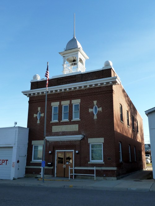 Historic brick city hall building with a clock tower and American flag, set against a clear blue sky.