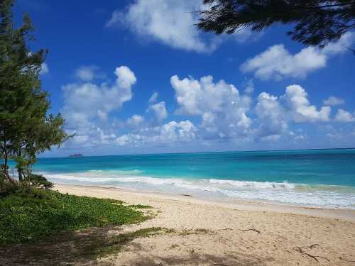 A serene beach scene with turquoise water, white sand, and fluffy clouds under a bright blue sky.