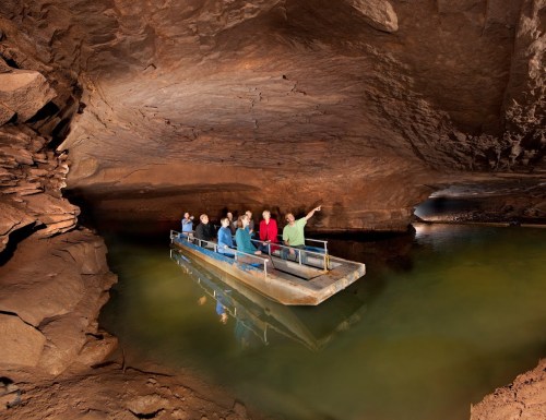 A group of people on a boat exploring a dark cave with water and rock formations.