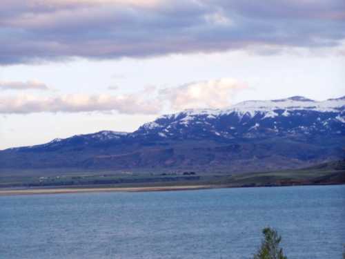 A serene lake with mountains in the background, partially covered in snow under a cloudy sky.