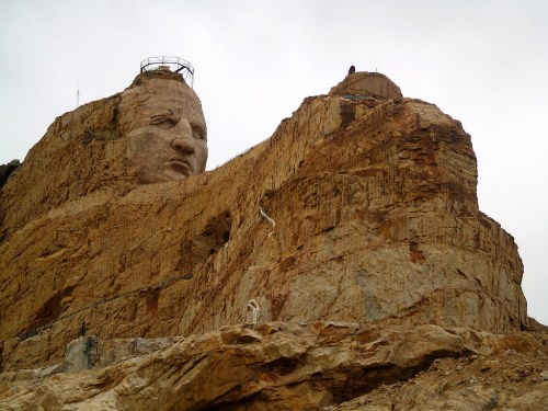 A large stone sculpture of a face carved into a rocky mountain, surrounded by rugged terrain and cloudy skies.