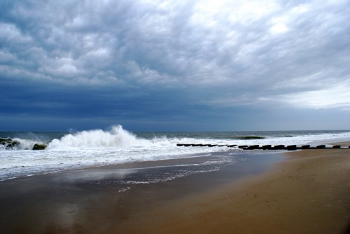 A stormy beach scene with dark clouds, crashing waves, and a sandy shore lined with wooden posts.