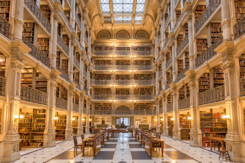 A grand library interior with tall bookshelves, elegant architecture, and warm lighting illuminating wooden tables.