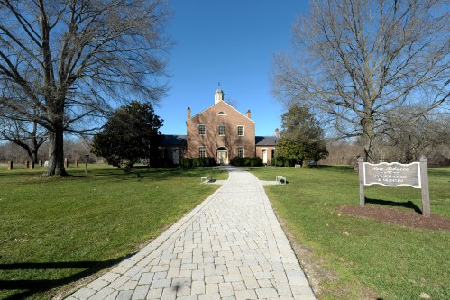 A brick building with a pathway leading to it, surrounded by trees and grass under a clear blue sky.