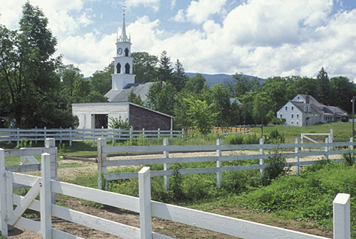 A scenic rural landscape featuring a church steeple, white fences, and lush greenery under a partly cloudy sky.