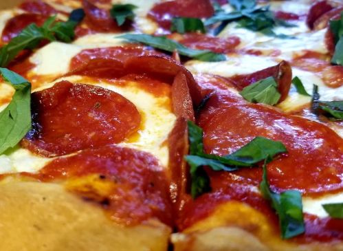 Close-up of a pepperoni pizza topped with fresh basil and melted cheese.