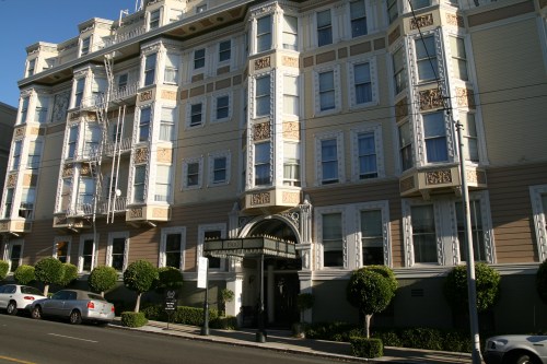 A historic building with ornate architecture, featuring balconies and neatly trimmed bushes in front.