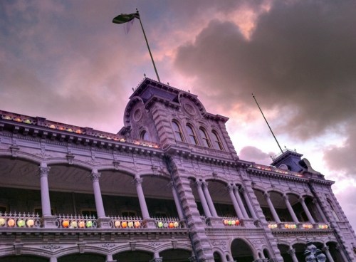 Historic building with ornate architecture, colorful lights, and a flag atop, set against a dramatic cloudy sky.
