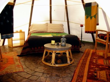 Cozy interior of a tent featuring a bed, table, and decorative rugs, creating a warm, inviting atmosphere.