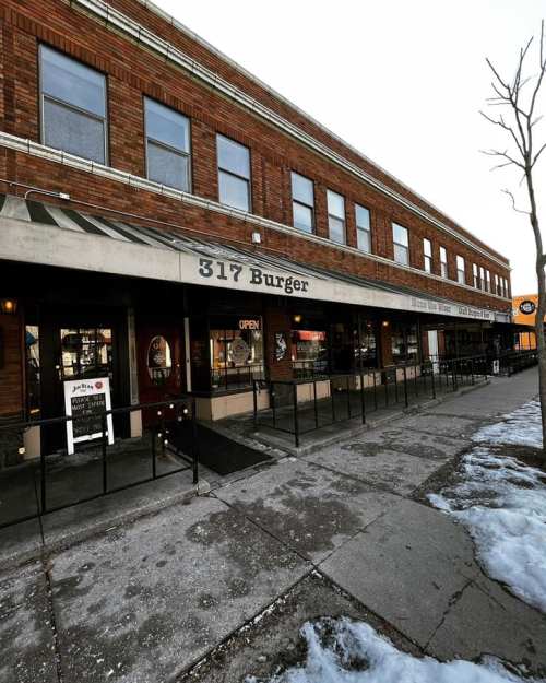 Exterior view of 317 Burger restaurant, featuring a brick facade and an "OPEN" sign, with snow on the ground.