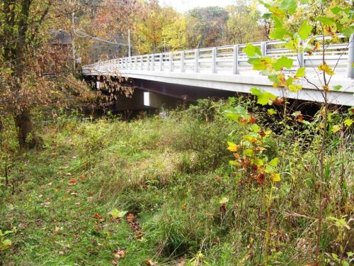 A bridge spans over a grassy area with autumn foliage and trees in the background.