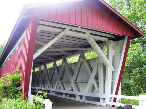 A red and white covered bridge with a wooden structure, surrounded by greenery.