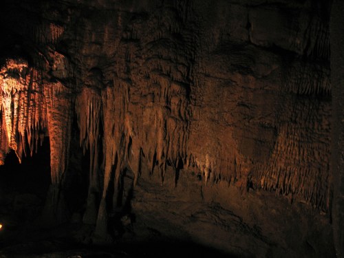 Stalactites and stalagmites in a dimly lit cave, showcasing textured rock formations and natural beauty.