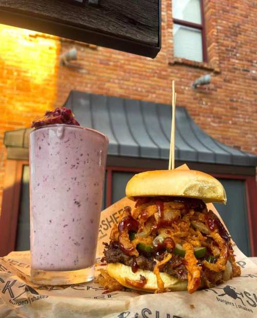 A juicy burger topped with crispy onions and barbecue sauce, alongside a berry milkshake in a glass.